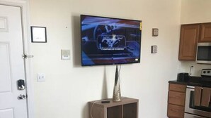 Una sala de estar con un televisor de pantalla plana montado en la pared, una mesa de centro de madera y una cocina con armarios y electrodomésticos de madera.