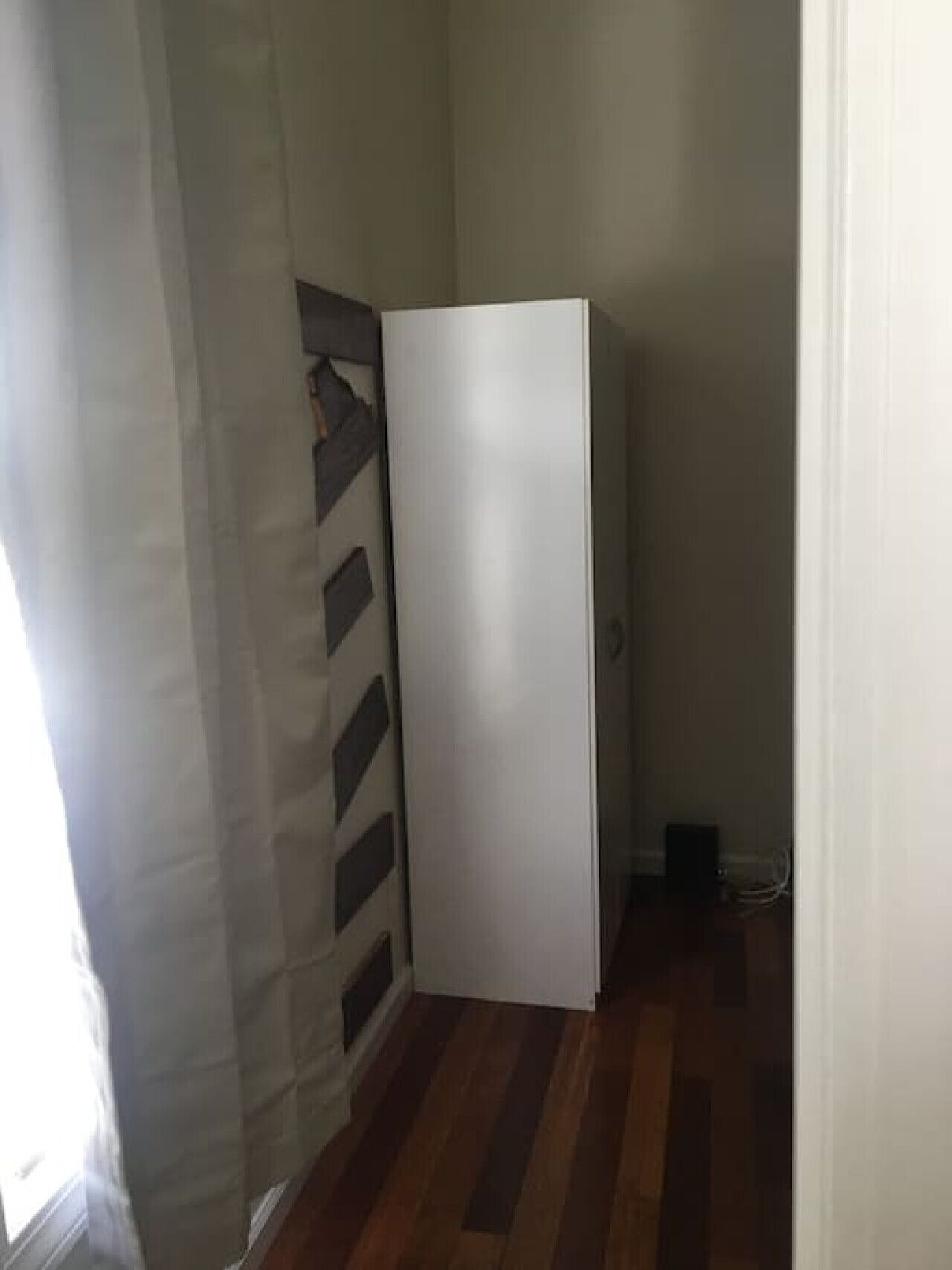Un pasillo estrecho con una puerta blanca, piso de madera y un diseño decorativo en la pared.