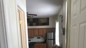 Un pasillo estrecho con suelo de madera que conduce a una zona de cocina con armarios de madera y un refrigerador.