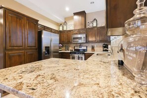 Cucina con ripiani in granito, mobili in legno, elettrodomestici in acciaio inossidabile e un barattolo di vetro grande a destra.