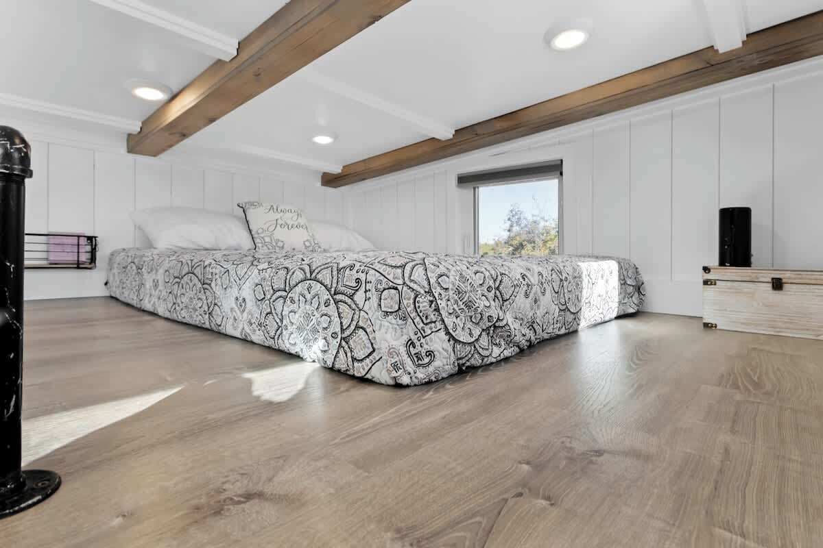 A bedroom with a patterned bedspread, wooden beams, a window, and a bedside table.
