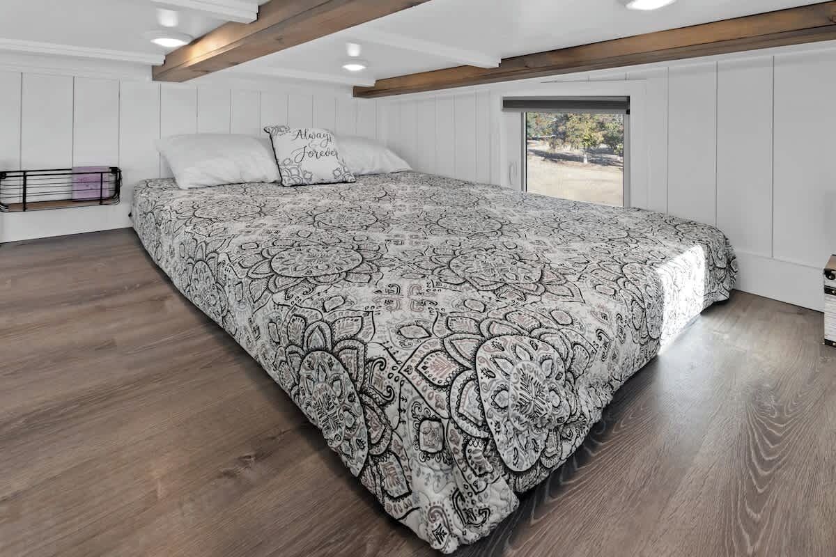 A bedroom with a large bed, white walls, wooden beams, and a window with a view.