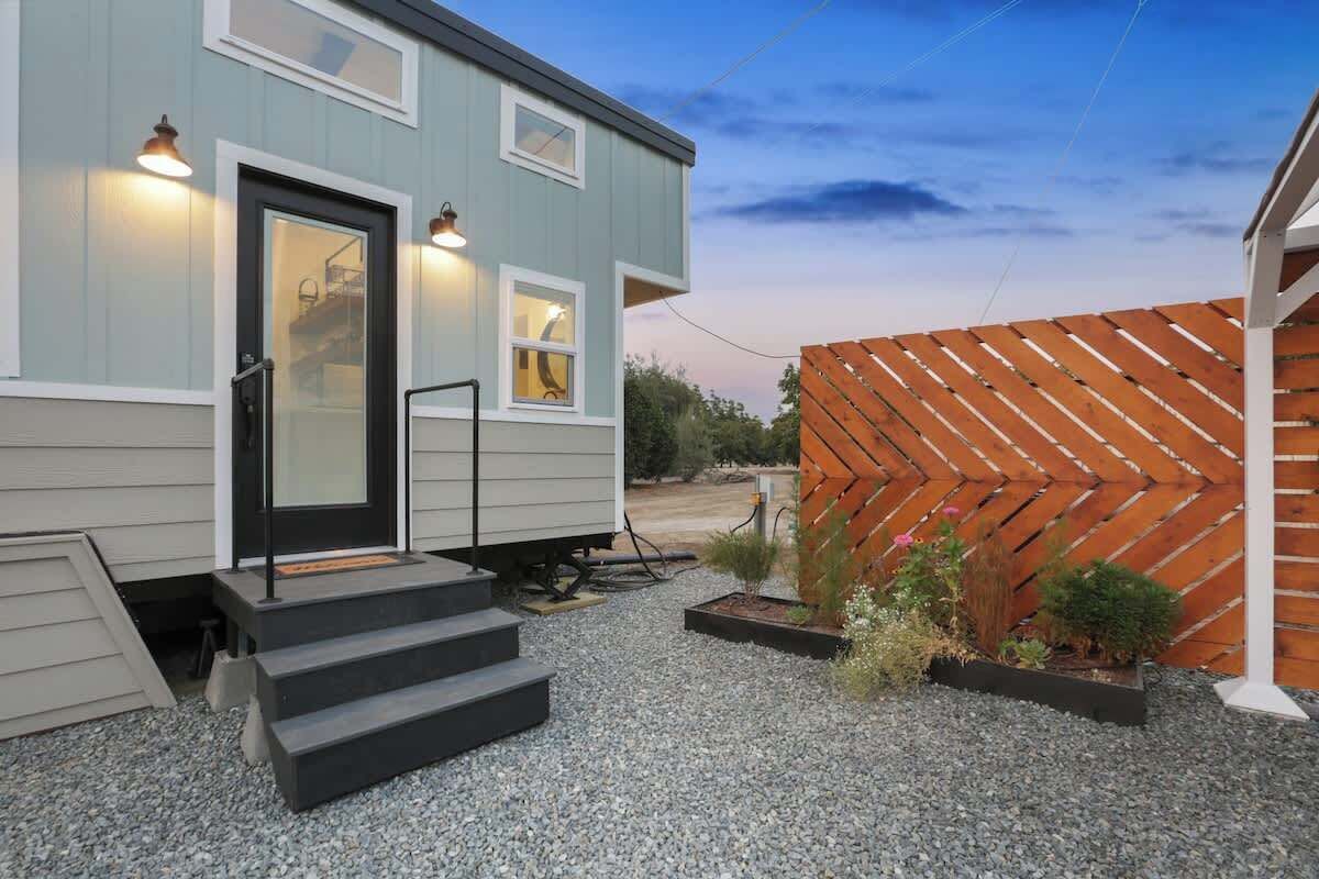 A two-story house with a front door, steps, and a small garden area with plants and a wooden fence.
