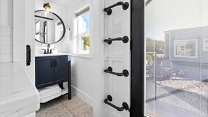 A bathroom with a white vanity, a round mirror, and a window with blinds. - Charming Tiny Home in Olive Grove - Near Sequoias (Lindsay)