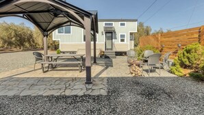 A covered outdoor seating area with a picnic table and chairs, a wooden fence, and a building in the background. - Charming Tiny Home in Olive Grove - Near Sequoias (Lindsay)