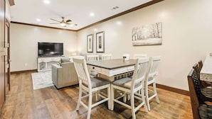 Un comedor con una mesa y sillas de madera, un televisor y obras de arte enmarcadas en la pared.