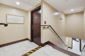 Un pasillo de hotel con piso de mármol, una puerta de madera con el número 201, una barandilla y un detector de incendios.