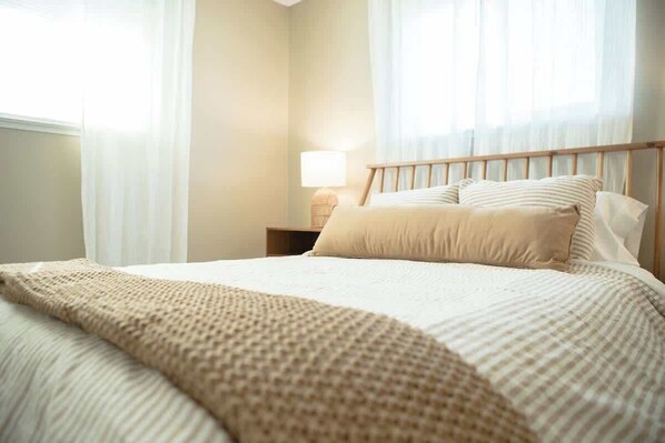 Una cama bien hecha con una colcha a rayas, cabecera de madera y una lámpara de noche.