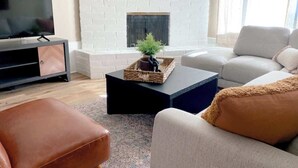 A living room with a white brick fireplace, a flat-screen TV, a black coffee table, and a beige sofa.