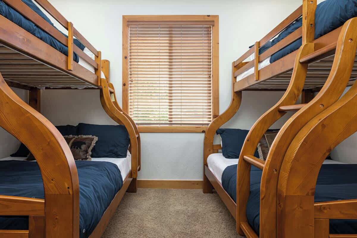 A room with two bunk beds, a window with blinds, and a carpeted floor.