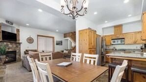 A spacious living area with a fireplace, a dining table with chairs, a kitchen with wooden cabinets, and a chandelier.