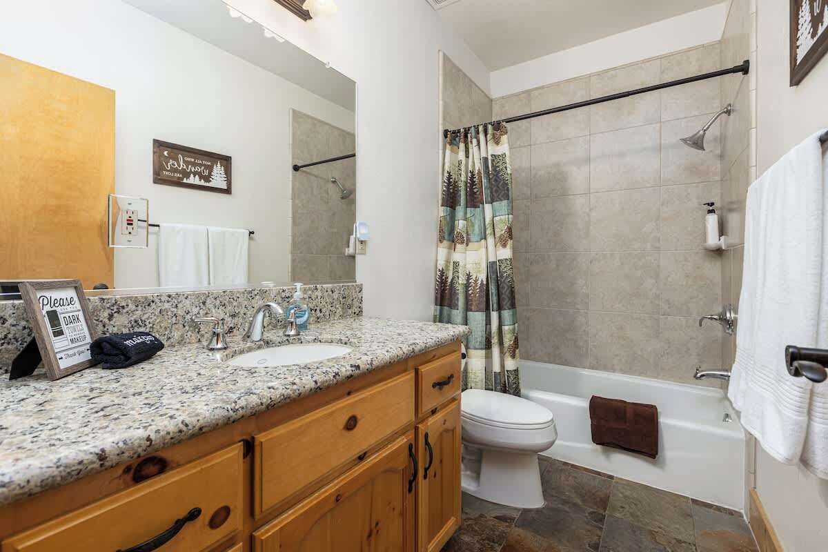 A bathroom with a granite countertop, two sinks, a toilet, and a bathtub.