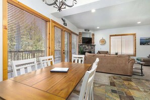 Cozy living area with a dining table, sofa, and television, featuring a fireplace and large windows.