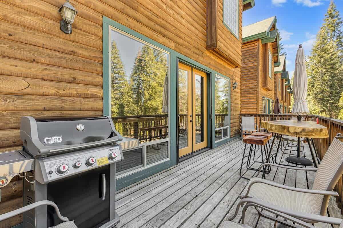 Une cabane en bois dotée d’un barbecue, de meubles de jardin et d’une terrasse offrant une vue sur la forêt.