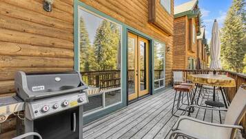 Une cabane en bois dotée d’un barbecue, de meubles de jardin et d’une terrasse offrant une vue sur la forêt.