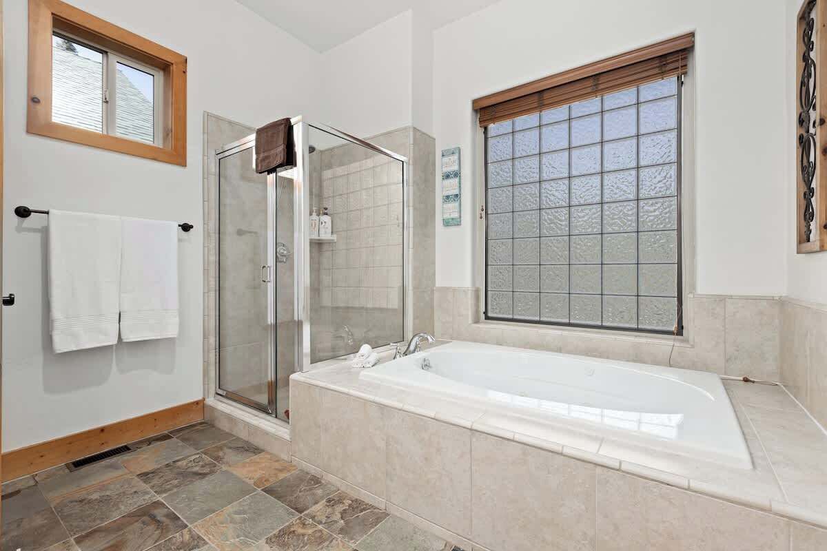 Une salle de bain moderne dotée d’une douche à parois de verre, d’une grande baignoire et d’une fenêtre avec du verre dépoli.