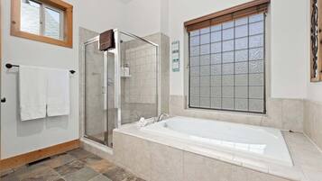 Une salle de bain moderne dotée d’une douche à parois de verre, d’une grande baignoire et d’une fenêtre avec du verre dépoli.