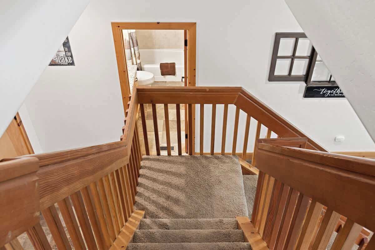 A wooden staircase with a carpeted landing leading to a bathroom with a bathtub and a towel rack.