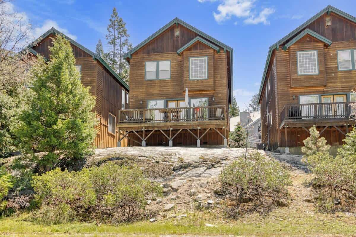 Une cabane en bois dotée d’un balcon, entourée d’une végétation luxuriante et d’un paysage rocheux.