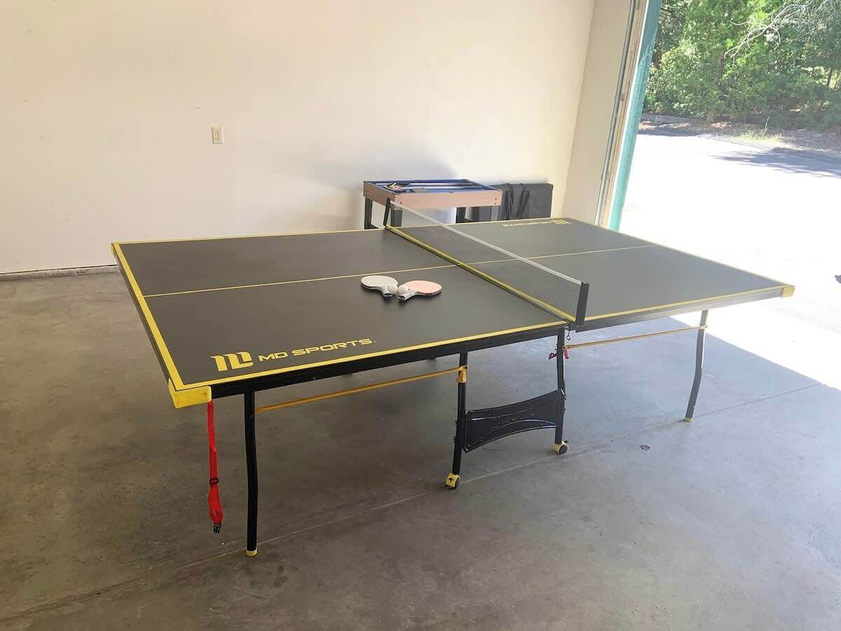 Een tafeltennistafel met een net in het midden, geplaatst in een ruimte met een betonnen vloer en een raam aan de rechterkant.