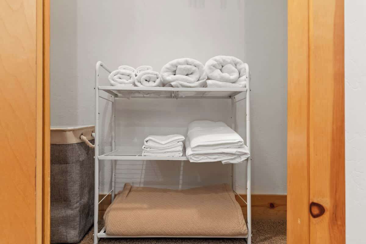 Una cama litera de metal blanco con toallas blancas y una manta color beige.