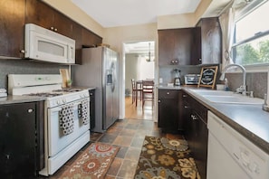 A kitchen with a stove, microwave, refrigerator, and dishwasher. There is a dining area visible in the background.