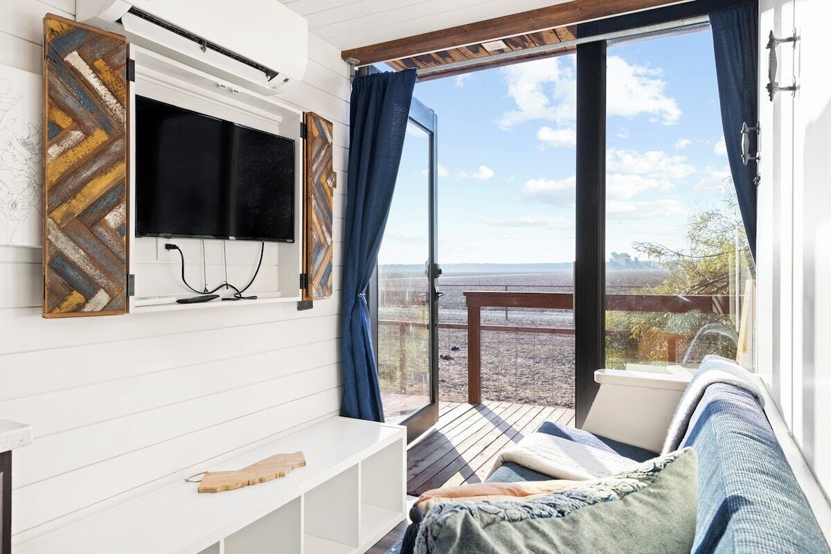A room with a television mounted on the wall, a sofa, and a view of the outdoors.