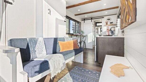 A modern living room with a sofa, a coffee table, and a rug. There is a kitchen area in the background. - Tiny Cargo Home, Farm Experience with Rooftop Views (Tulare)