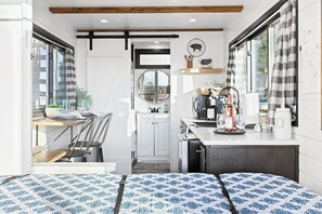 A compact kitchen with a dining area, a bed with patterned bedding, and a view through a window. - Tiny Cargo Home, Farm Experience with Rooftop Views (Tulare)