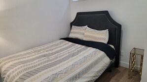 A neatly made bed with patterned bedding, a dark headboard, and a small bedside table with a gold frame. - Two Bedrooms Modern Cozy Suite (Ardrossan)