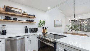 A modern kitchen with white cabinetry, stainless steel appliances, wooden shelves, and a large window.