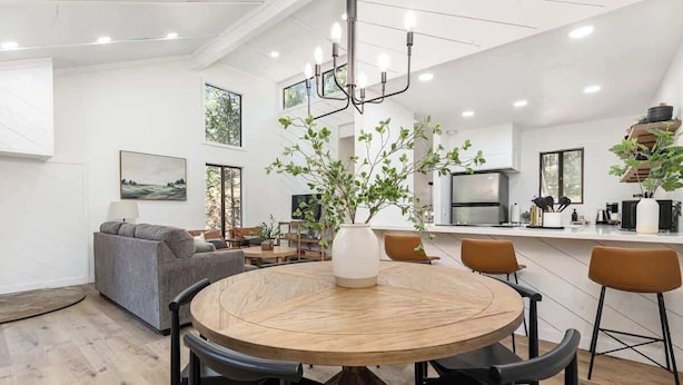 A modern kitchen with a central island, a dining area with a round wooden table, and a living room with a sofa and a coffee table.