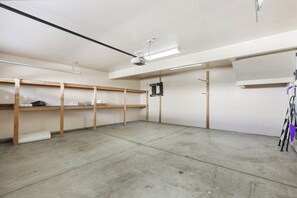 A spacious room with concrete flooring, wooden shelving units, and a ceiling-mounted projector. - Slice of Paradise Steps to Morro Rock (Morro Bay)