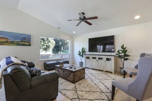 Een moderne woonkamer met een bank, fauteuil, salontafel en een flatscreen televisie aan de muur.