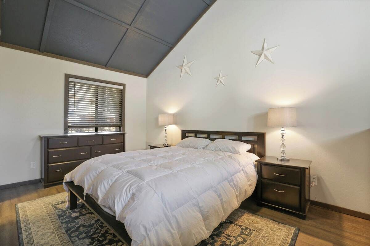 A bedroom with a bed, bedside tables, a window with blinds, and wall decorations.