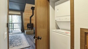 A room with a wooden door, a white appliance, and a view of a wooden cabin with a chimney. - Shaver Escape! Mountain Loft Condo (Shaver Lake)