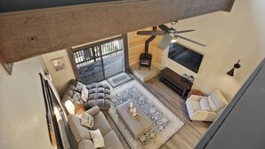 A modern living room with a sectional sofa, a coffee table, a TV, and a ceiling fan. - Shaver Escape! Mountain Loft Condo (Shaver Lake)