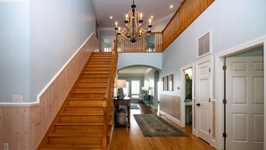 A spacious hallway with a wooden staircase, a chandelier, and a view into the living area. - Oceanfront Showplace w/ Private Pool & Elevator; Expansive Beach & Ocean Views; Multiple Porches (Edisto Island)