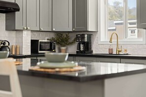 A modern kitchen with grey cabinets, a black countertop, a microwave, a coffee maker, and a window with a view of the outside.