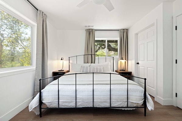 A bedroom with a bed, two bedside tables, a window with curtains, a door, and a ceiling fan. - Riverfront Gateway to Sequoia NP (Three River)