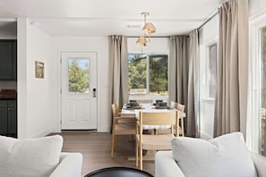 A dining area with a table set for four, a sofa, and a view of trees through the window. - Riverfront Gateway to Sequoia NP (Three River)