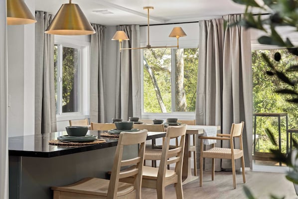 A dining area with a black countertop, wooden chairs, and pendant lights.