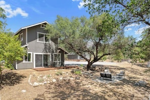 A two-story house with a patio area, a tree, and outdoor furniture.