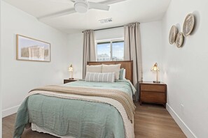 A bedroom with a bed, two bedside tables, a ceiling fan, a window with curtains, and wall art.