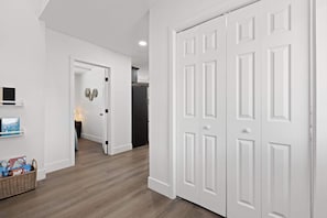 A hallway with a wooden floor, white walls, and a closed white door.