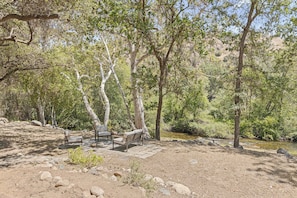 A natural setting with a wooden bench and a picnic table surrounded by rocks and trees.