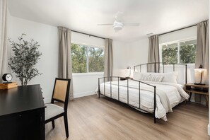 A bedroom with a bed, a desk, a chair, a plant, and a window with curtains.