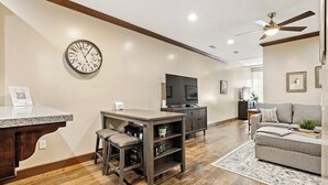 A modern living room with a wooden floor, a grey sofa, a coffee table, a TV, and a clock on the wall. - Midtown Loft 301 on Main St DT Visalia (Visalia)