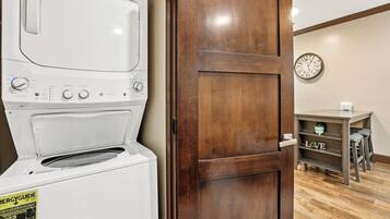 A laundry area with a white washer and dryer, a wooden door, a clock on the wall, and a shelf with the word 'LOVE' on it.