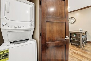 A laundry area with a white washer and dryer, a wooden door, a clock on the wall, and a shelf with the word 'LOVE' on it. - Midtown Loft 301 on Main St DT Visalia (Visalia)